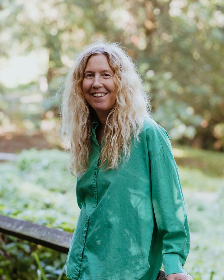 Anne-Marie leaning on a wooden rail in the woods, smiling